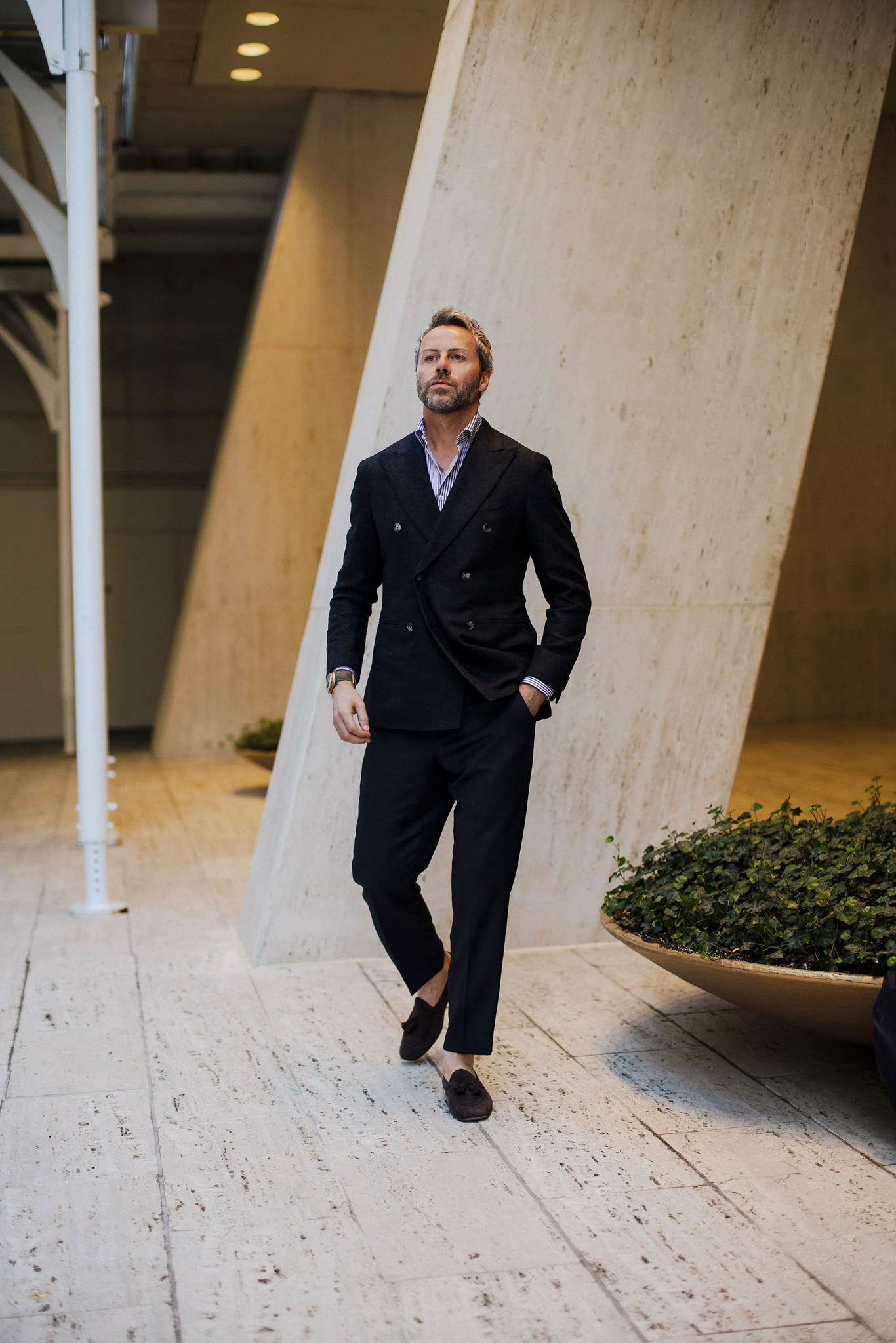 Gilberto Ramerini in a navy double-breasted blazer and suede loafers, walking through a stone courtyard