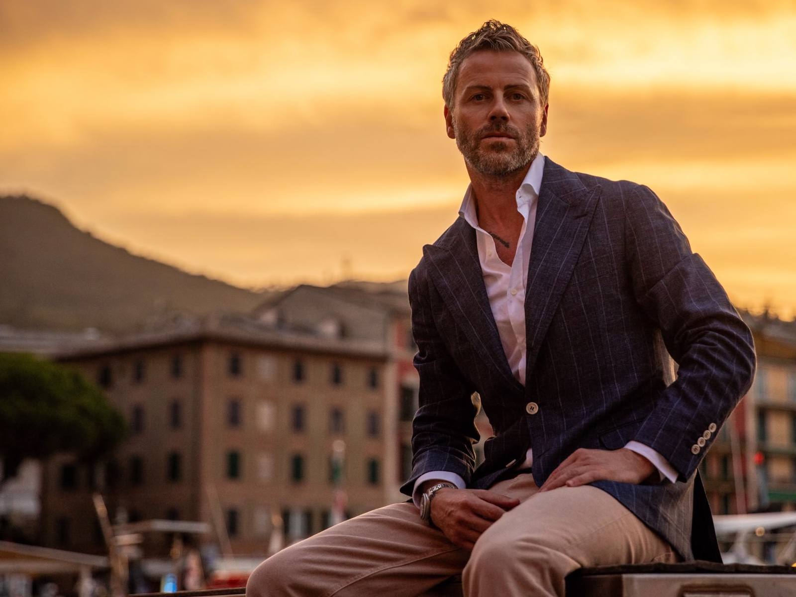 Gilberto Ramerini seated at sunset, in a pinstripe blazer